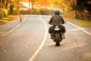 Man riding a motorcycle down a road in autumn