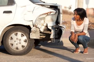 Woman crouching down and looking at damage to her car