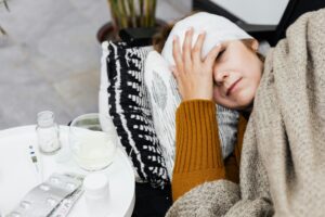 Woman laying in a bed and putting her hand to her head with a large bandage