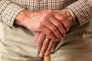 An older man holding his hand and grasping a cane