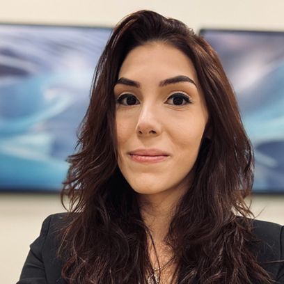 Woman with long dark hair smiles in front of abstract blue artwork. She wears a black blazer.