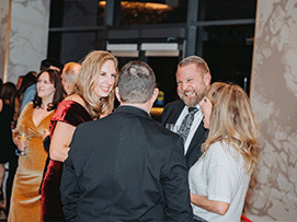 Group of four people chatting at a formal event, with elegant attire and a stylish venue backdrop.