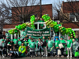 Group of people in green attire celebrating with balloons and a banner reading 