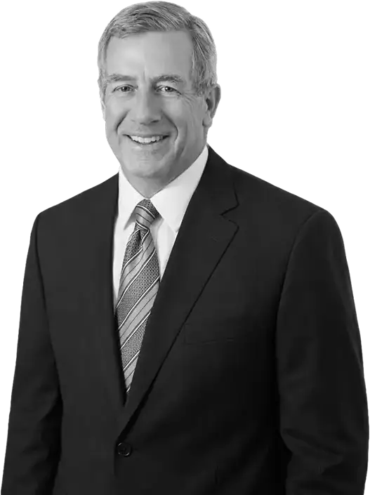 Smiling man in a dark suit and striped tie, standing against a plain background.